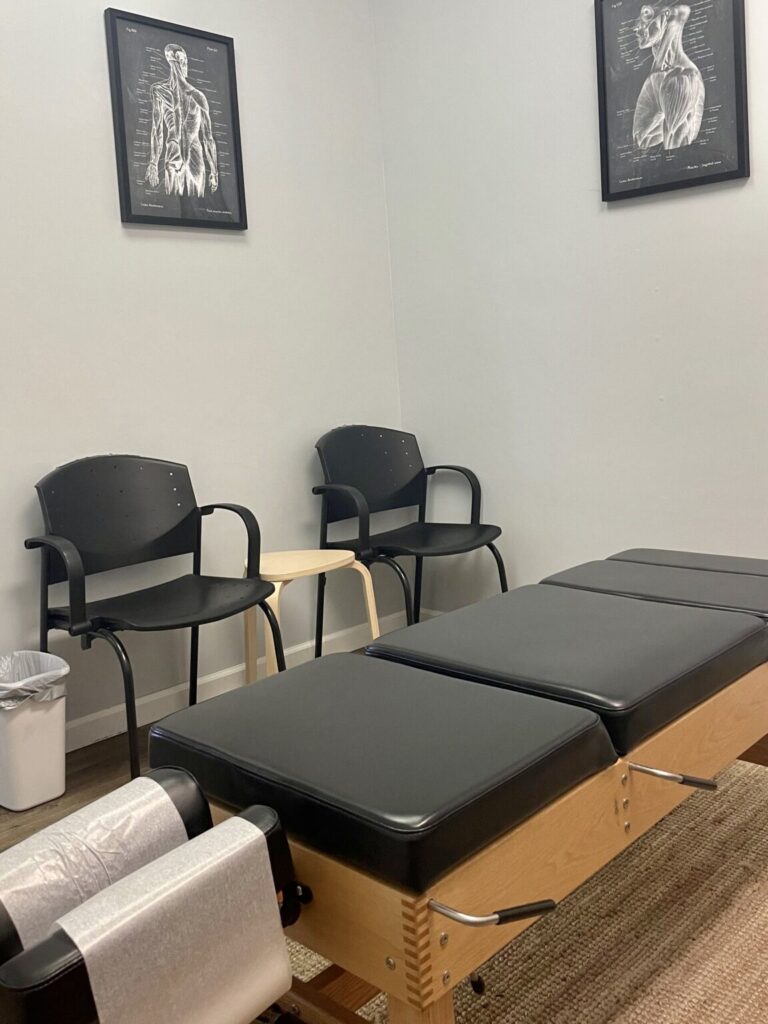 chiropractor table with two chairs and chalkboard anatomy photos on wall in treatment office of Steadfast Spine and Sport Warrenton MO